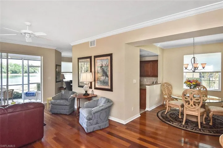 Living area with dark wood finished floors, baseboards, visible vents, ceiling fan with notable chandelier, and crown molding