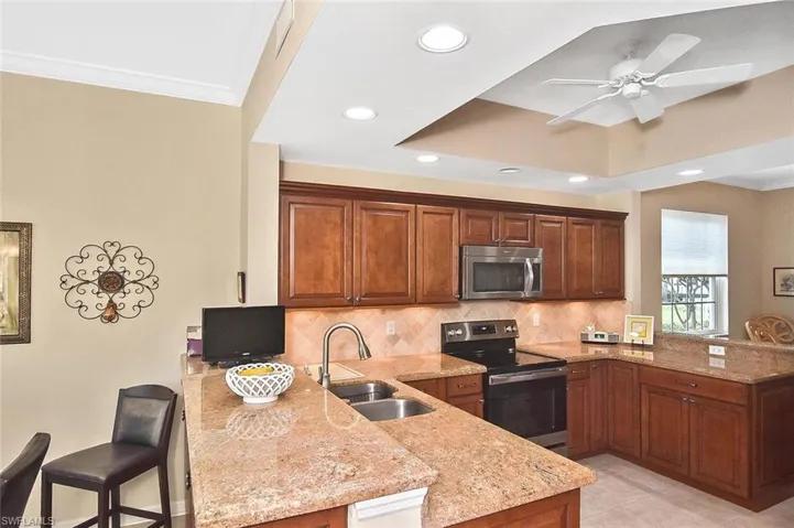 Kitchen with light stone counters, a sink, stainless steel appliances, a peninsula, and ornamental molding