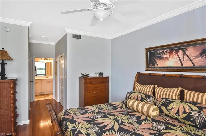 Bedroom with crown molding, ensuite bathroom, ceiling fan, dark wood-type flooring, and visible vents
