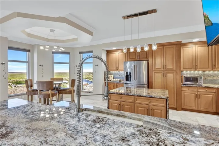 Kitchen with decorative backsplash, hanging light fixtures, stainless steel fridge with ice dispenser, light stone countertops, and crown molding