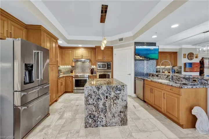 Kitchen with tasteful backsplash, hanging light fixtures, appliances with stainless steel finishes, light stone countertops, and a center island