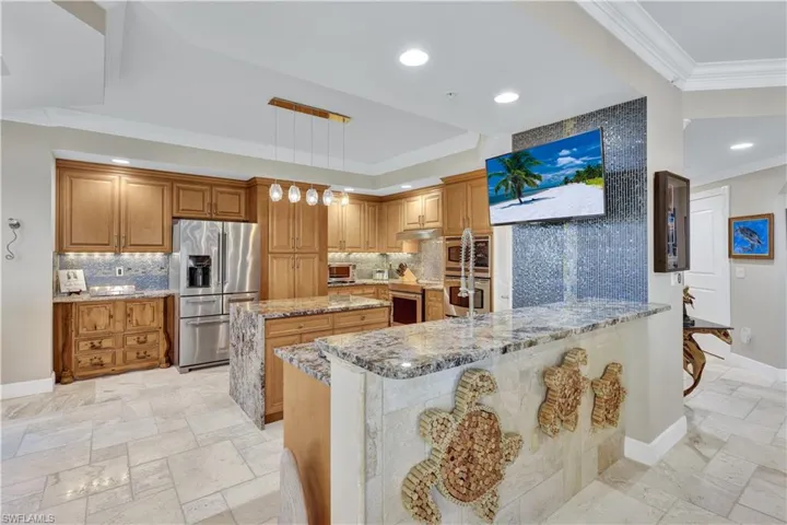 Kitchen featuring stainless steel appliances, a large island, light stone countertops, pendant lighting, and tasteful backsplash