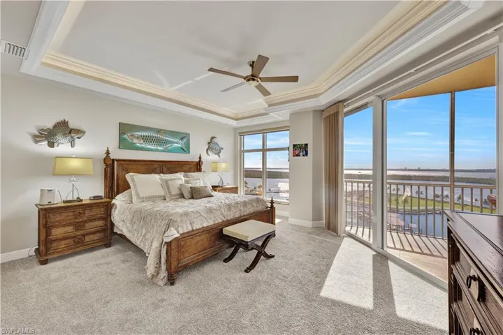Bedroom featuring light colored carpet, a tray ceiling, a water view, and ceiling fan