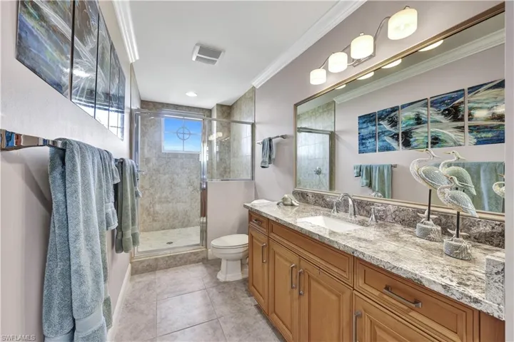 Bathroom with toilet, tile patterned flooring, a shower with shower door, ornamental molding, and vanity