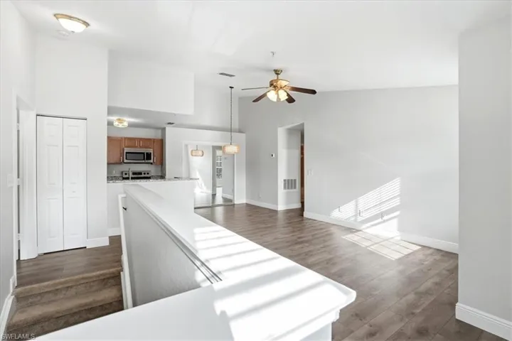 Kitchen featuring a high ceiling, dark wood-style flooring, wood finish cabinetry, decorative light fixtures, and stainless steel appliances