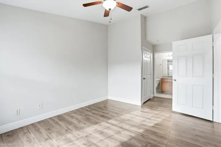 Unfurnished bedroom with ensuite bathroom, light wood finished floors, and a ceiling fan
