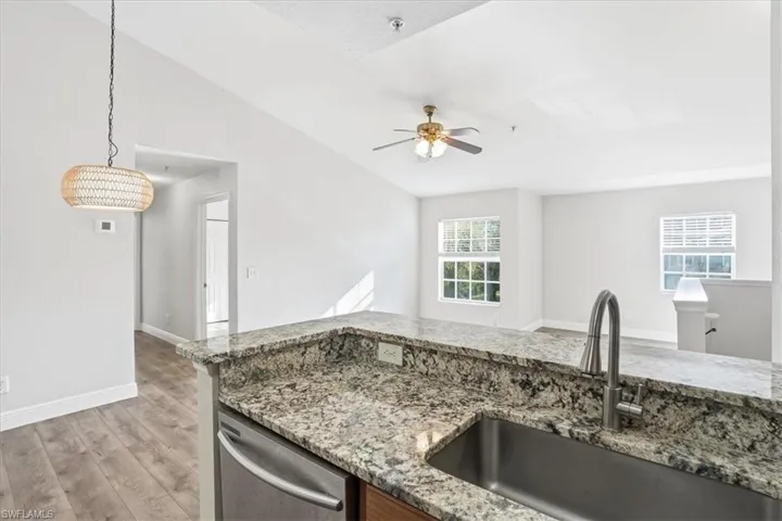 Kitchen featuring light stone countertops, light wood-type flooring, vaulted ceiling, dishwasher, and a ceiling fan