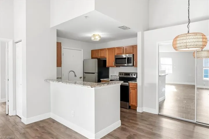 Kitchen featuring stainless steel appliances, wood finish cabinetry, light stone counters, a peninsula, and a high ceiling
