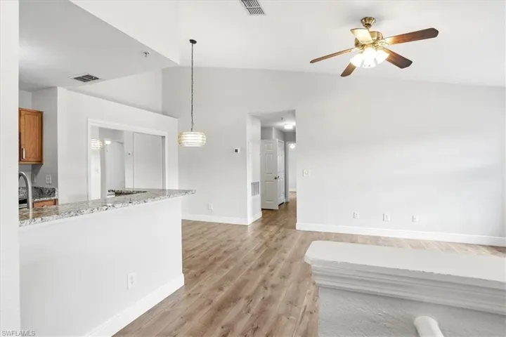 Kitchen featuring light stone countertops, vaulted ceiling, light wood finished floors, hanging light fixtures, and ceiling fan