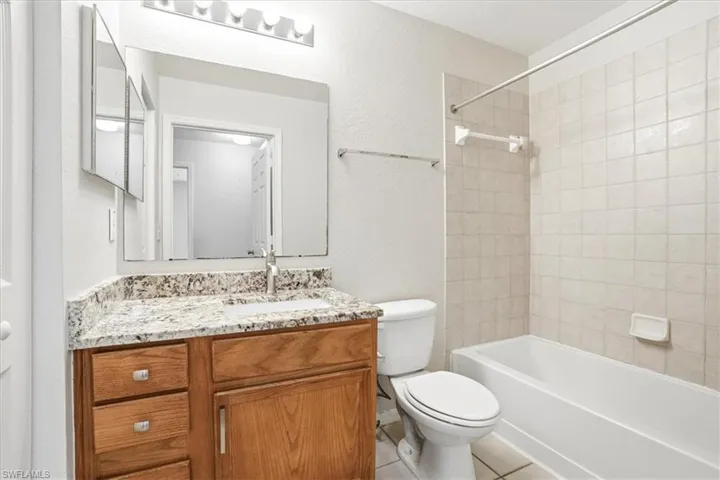 Bathroom featuring a textured wall, vanity, bathtub / shower combination, and light tile patterned floors