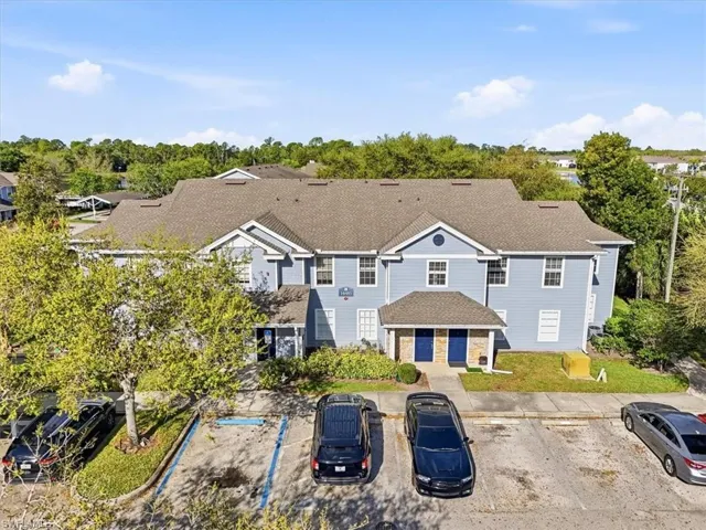 View of front of property featuring roof with shingles, uncovered parking, view of wooded area, and stone siding