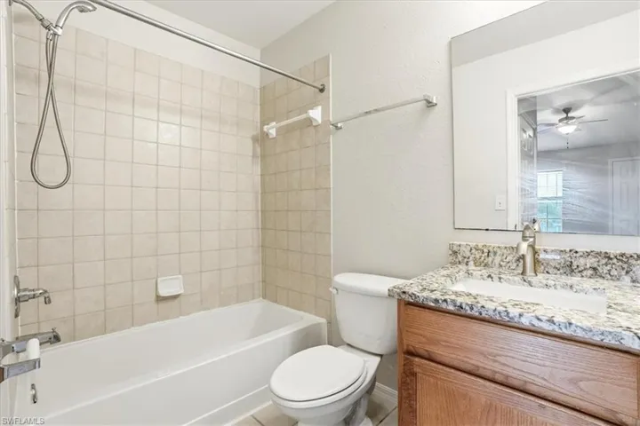 Bathroom with a textured wall, vanity, bathing tub / shower combination, and ceiling fan