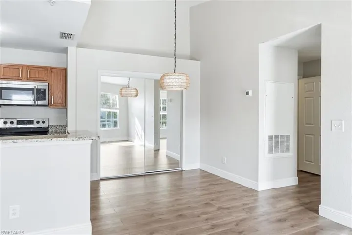 Kitchen with stainless steel appliances, light stone counters, light wood-style floors, wood finish cabinets, and decorative light fixtures
