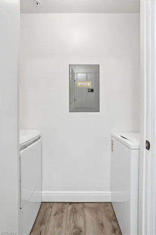Laundry room with electric panel, light wood-type flooring, and washing machine and dryer