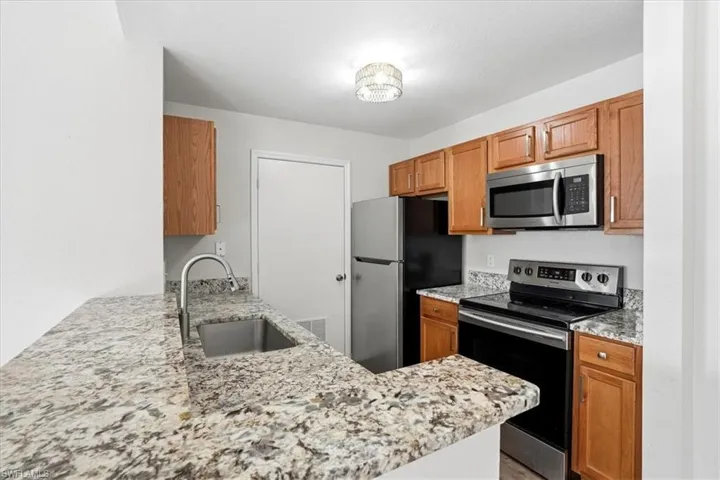 Kitchen with stainless steel appliances, light stone countertops, wood finish cabinets, and a peninsula