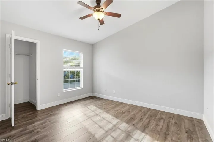 Unfurnished bedroom featuring a walk in closet, ceiling fan, and wood finished floors