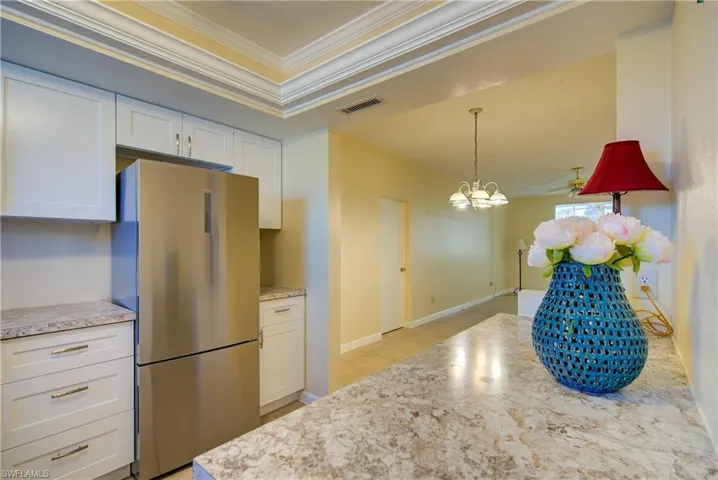 Kitchen featuring freestanding refrigerator/freezer, white cabinetry, ornamental molding, and attractive laminate counters.