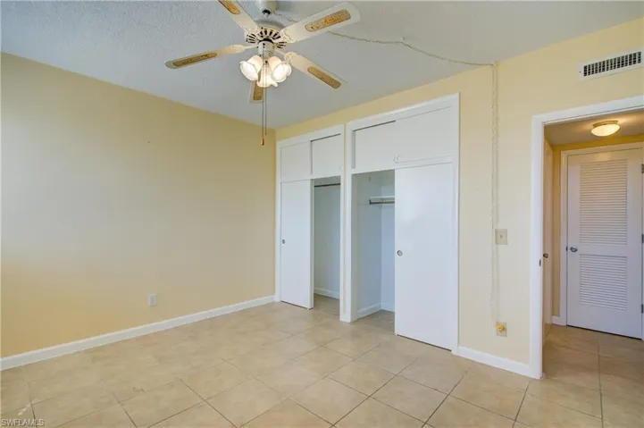 Unfurnished bedroom with two closets,ceiling fan, and light tile patterned flooring