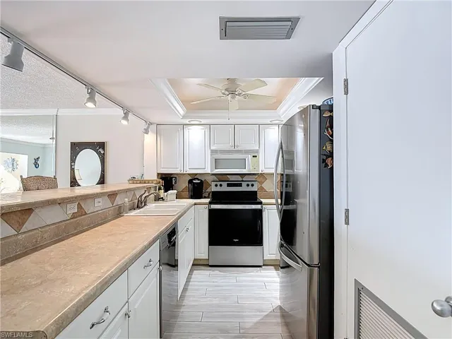 Kitchen with crown molding, white cabinets, stainless steel appliances, light countertops, and decorative backsplash