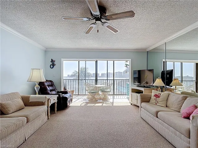 Carpeted living area featuring a ceiling fan, plenty of natural light, a textured ceiling, and ornamental molding