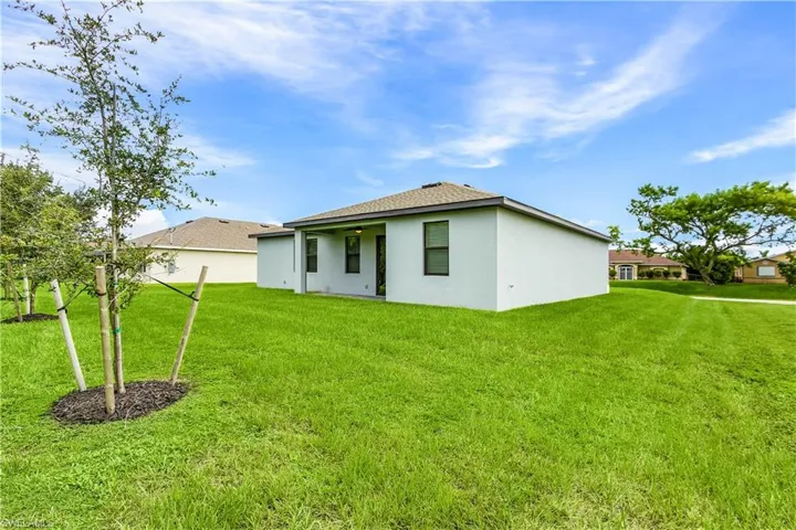 Back of property featuring a yard, stucco siding, and a shingled roof
