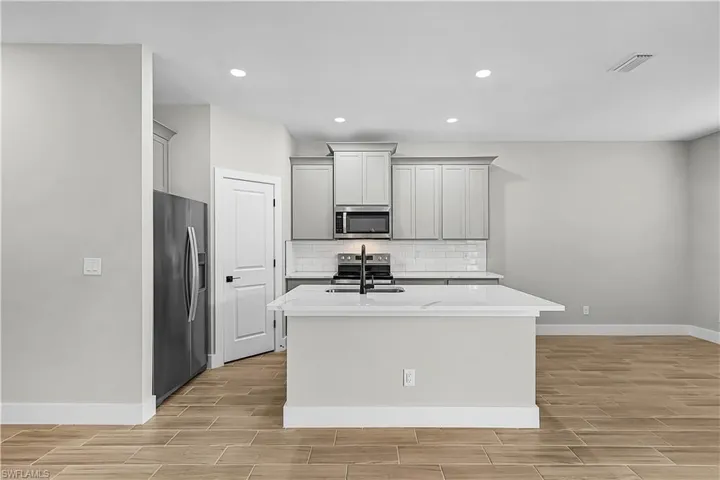 Kitchen featuring stainless steel appliances, gray cabinetry, a center island with sink, wood finish floors, and recessed lighting