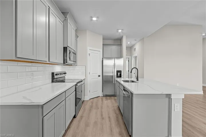 Kitchen with appliances with stainless steel finishes, wood tiled floors, gray cabinetry, backsplash, and a kitchen island with sink