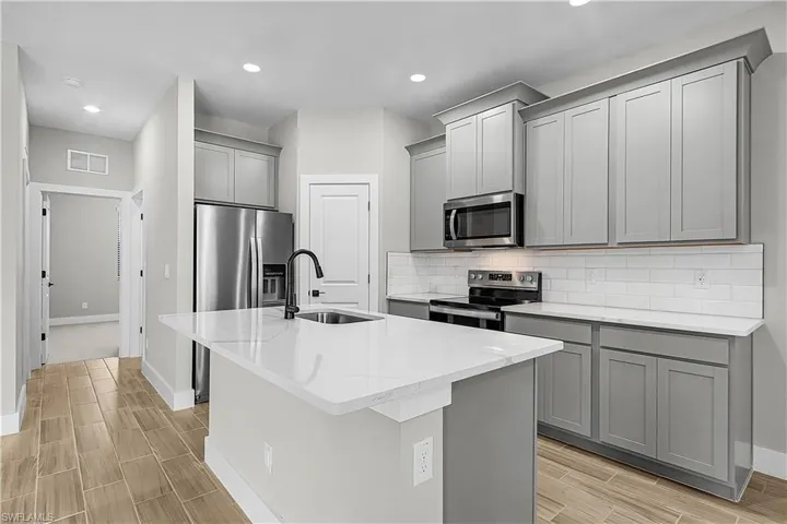 Kitchen with gray cabinets, appliances with stainless steel finishes, a kitchen island with sink, decorative backsplash, and wood finish floors