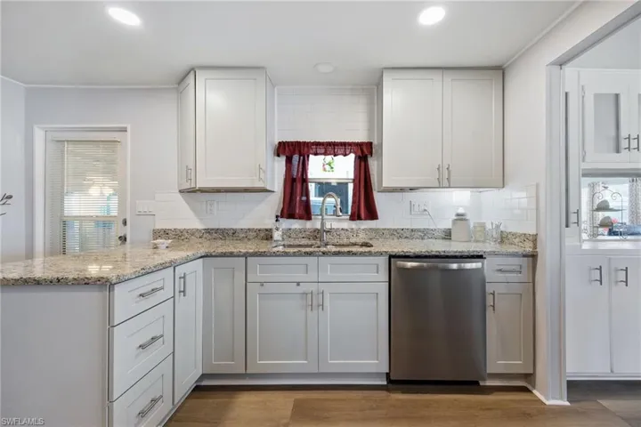 Kitchen featuring stainless steel dishwasher, light stone counters, white cabinets, tasteful backsplash, and recessed lighting