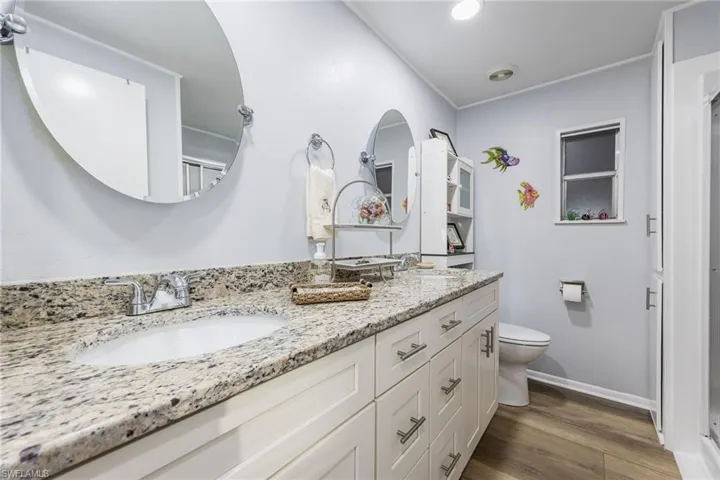 Bathroom with double vanity, dark wood-type flooring, and an enclosed shower