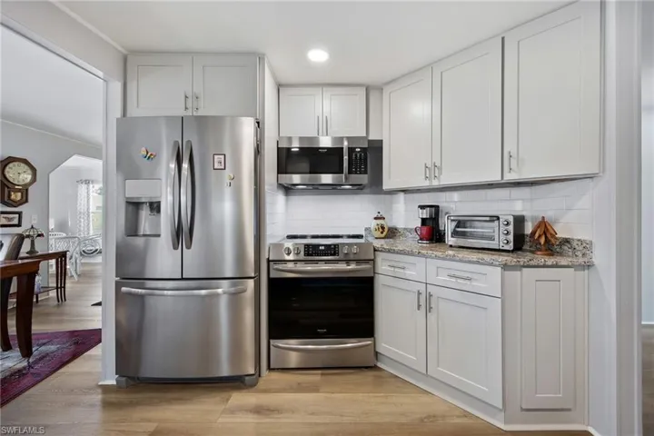 Kitchen featuring appliances with stainless steel finishes, light stone counters, tasteful backsplash, light wood finished floors, and recessed lighting