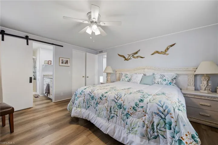 Bedroom featuring wood finished floors, a barn door, ensuite bath, and ceiling fan