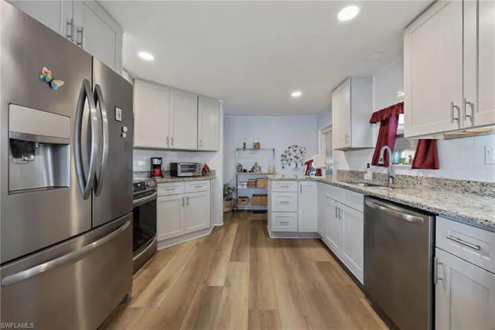 Kitchen featuring appliances with stainless steel finishes, decorative backsplash, light wood-type flooring, white cabinetry, and light stone counters