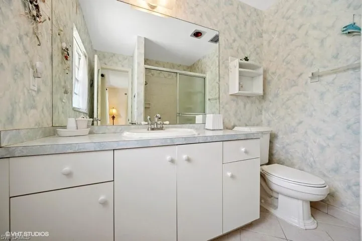 Full bathroom with wallpapered walls, toilet, tile patterned floors, and a shower stall