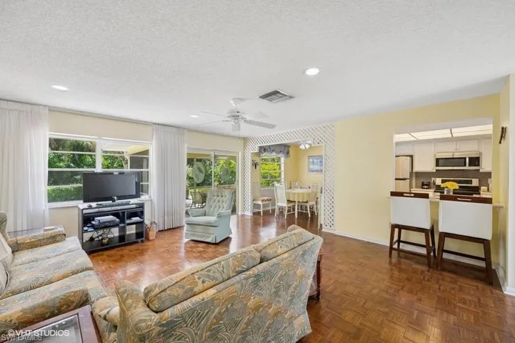 Living room with a textured ceiling, visible vents, a ceiling fan, and plenty of natural light