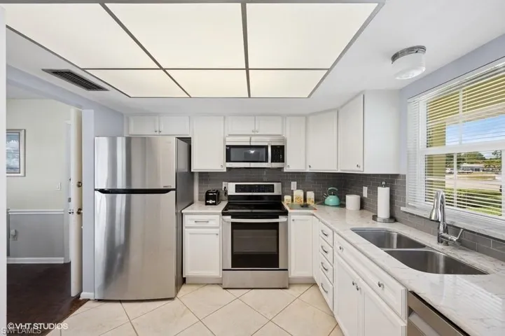 Kitchen featuring decorative backsplash, white cabinets, visible vents, appliances with stainless steel finishes, and a sink