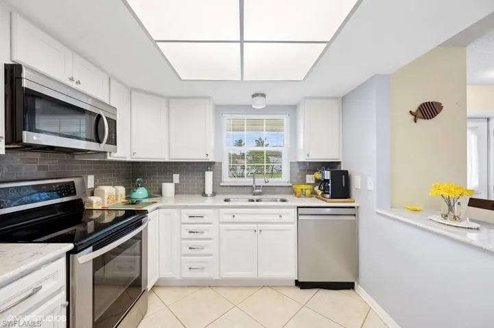 Kitchen with light tile patterned floors, stainless steel appliances, backsplash, a sink, and white cabinets