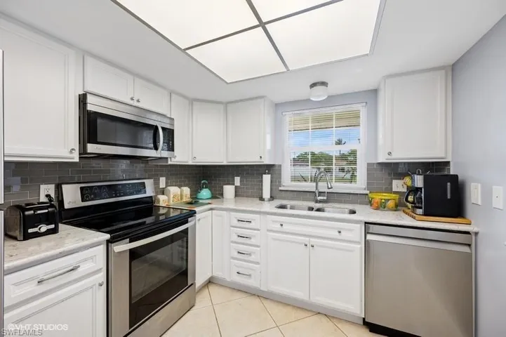 Kitchen featuring a sink, light tile patterned floors, stainless steel appliances, white cabinets, and decorative backsplash