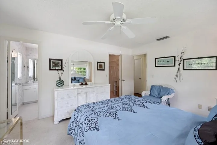 Bedroom with a textured ceiling, connected bathroom, visible vents, light carpet, and ceiling fan