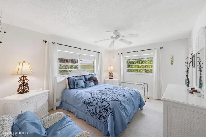 Bedroom featuring a ceiling fan, light colored carpet, and a textured ceiling