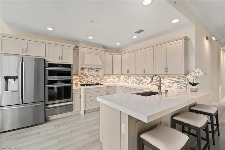 Kitchen with kitchen peninsula, backsplash, custom exhaust hood, appliances with stainless steel finishes, and sink