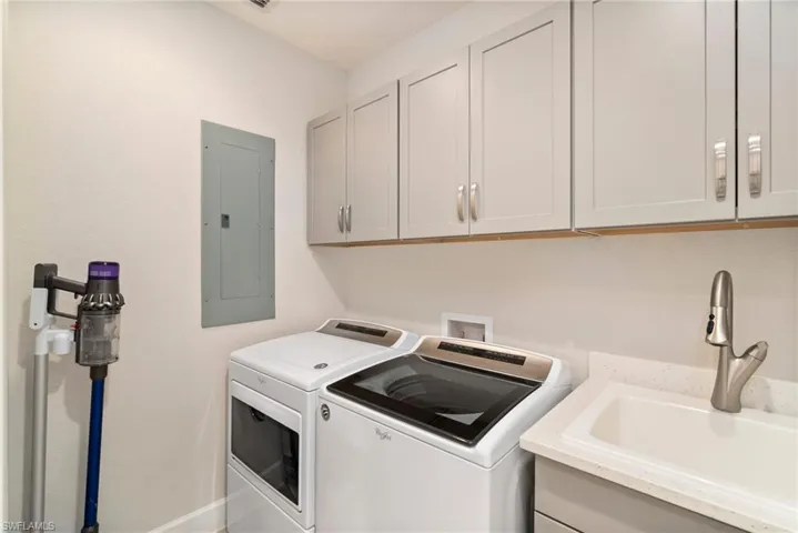 Clothes washing area featuring sink, cabinets, washer and dryer, and electric panel