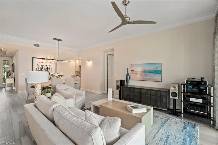Living room featuring ceiling fan with notable chandelier, wood-type flooring, and ornamental molding
