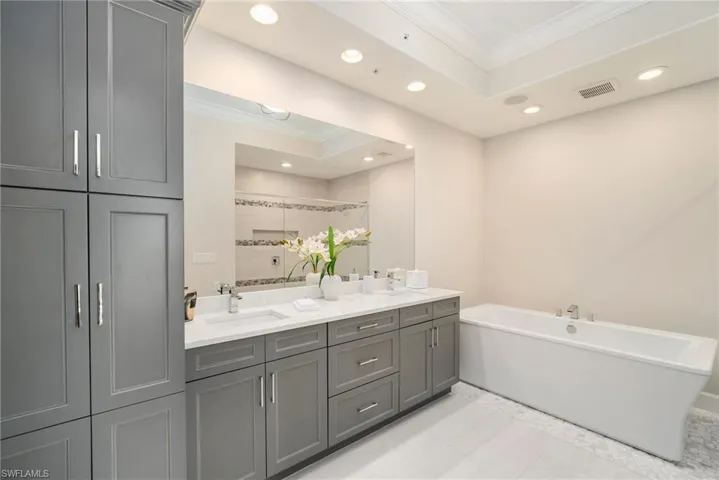 Bathroom featuring tile patterned floors, double sink vanity, ornamental molding, and a raised ceiling
