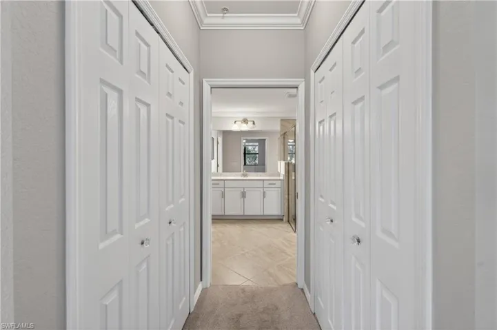 Hall with ornamental molding, light carpet, and light tile patterned floors