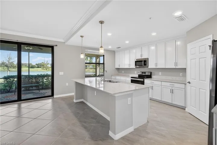 Kitchen featuring a water view, stainless steel appliances, a center island with sink, decorative light fixtures, and light stone counters