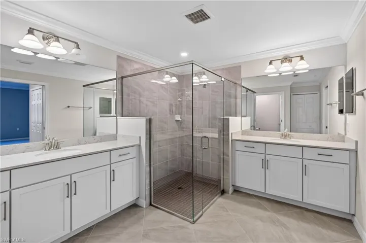 Full bath with ornamental molding, a shower stall, two vanities, light tile patterned floors, and recessed lighting