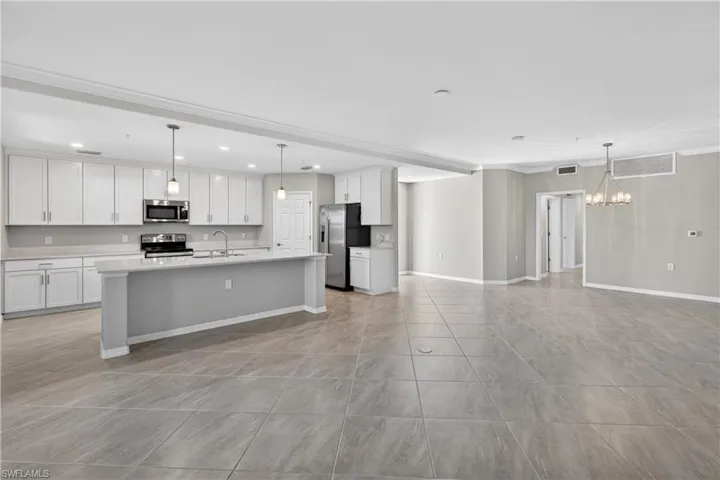 Kitchen featuring pendant lighting, open floor plan, an island with sink, white cabinetry, and stainless steel appliances