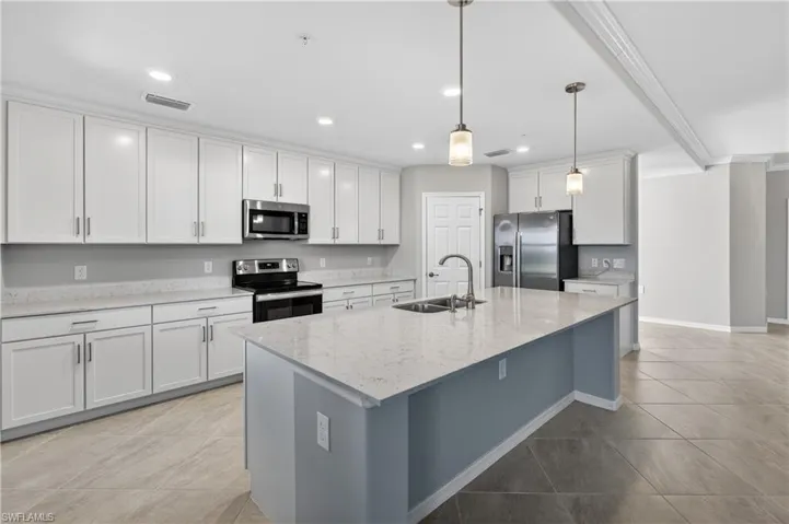 Kitchen featuring appliances with stainless steel finishes, pendant lighting, light stone counters, a kitchen island with sink, and white cabinets