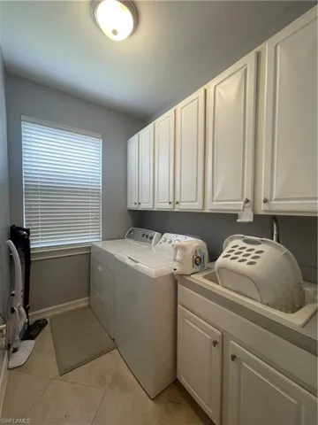 Washroom featuring light tile patterned floors, washer and clothes dryer, and cabinets